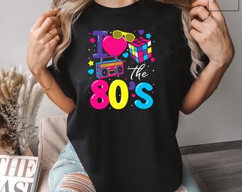 May include: Black t-shirt with a colorful graphic design featuring a heart with sunglasses, a Rubik's cube, a boombox, and the text "I love the 80's".