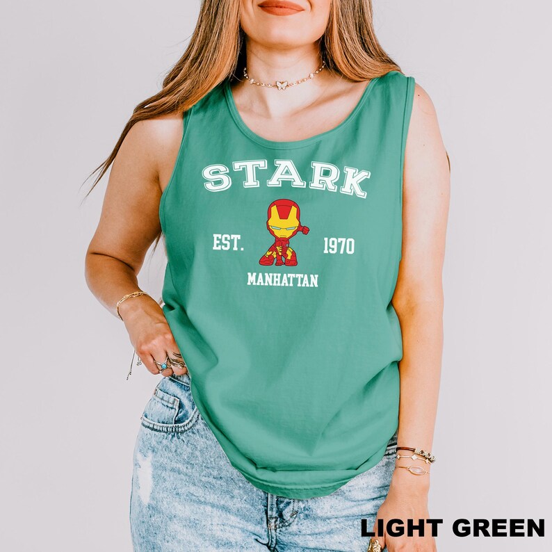 A woman wearing a green tank top with a graphic of a character from the Marvel Cinematic Universe, specifically Iron Man, and text that says "STARK EST. 1970 MANHATTAN".