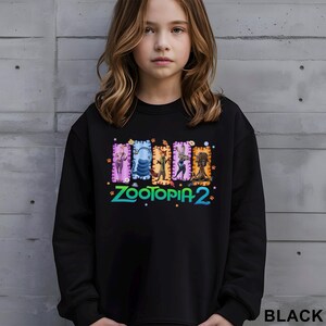 A young girl wearing a black sweatshirt with a colorful graphic design featuring characters from the animated film "Zootopia 2".
