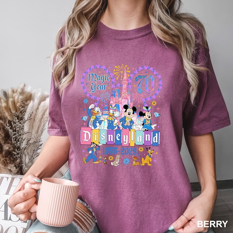 A woman wearing a purple t-shirt with a Disney theme graphic, including Mickey Mouse and other Disney characters, and text celebrating the 70th anniversary of Disneyland.