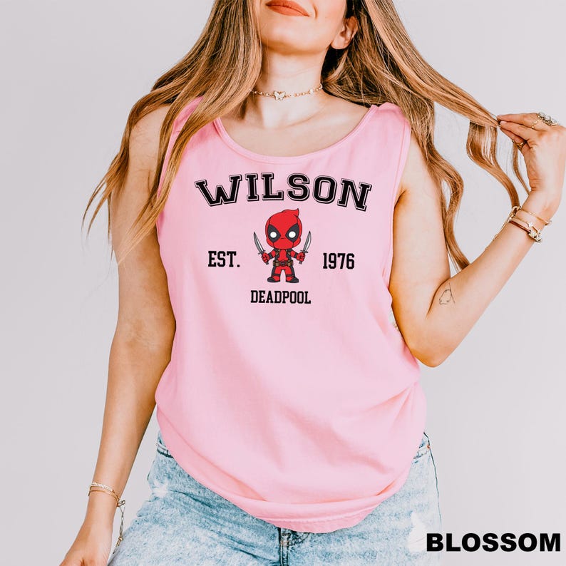 A woman wearing a pink tank top with a graphic of a character from the Marvel Cinematic Universe, specifically Deadpool.