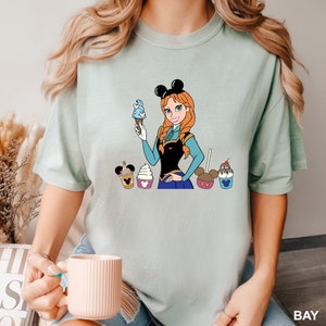 a woman holding a cup of coffee and a mickey mouse t - shirt