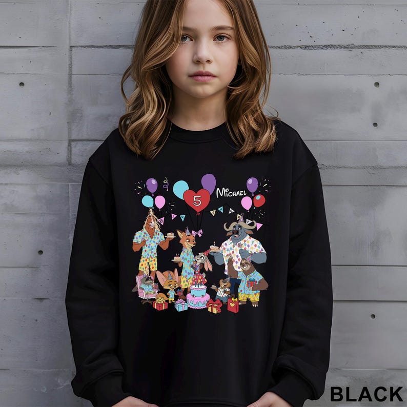 A young girl wearing a black sweatshirt with a colorful illustration of cartoon animals and a birthday party scene.