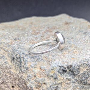 Op de afbeelding: Een zilveren ring met een grijze edelsteen. De ring heeft een gehamerde textuur en ligt op een grijze steen.