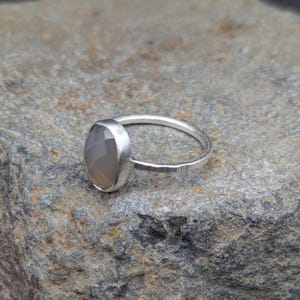 Op de afbeelding: Een zilveren ring met een grijze ovale edelsteen. De ring heeft een getextureerde band.