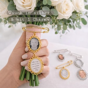 Könnte beinhalten: Ein goldfarbener Hochzeits-Gedenk-Charm mit zwei ovalen Rahmen, einer mit einem Foto und der andere mit Text, befestigt an einem Strauß weißer Rosen. Der Charm ist mit einer Sicherheitsnadel befestigt. Der Text im Bild lautet "Ich trage dich bei mir an meinem schönsten Tag".