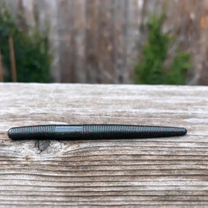 May include: A dark green and red worm-shaped fishing lure with a ribbed texture.