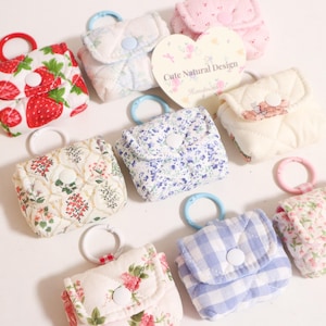 Pu&ograve; includere: Una collezione di piccole pochette in tessuto trapuntato con vari motivi, tra cui fragole, stampe floreali e quadretti vichy blu. Ogni pochette &egrave; dotata di chiusura a bottone automatico e di un anello circolare in plastica per appenderla.