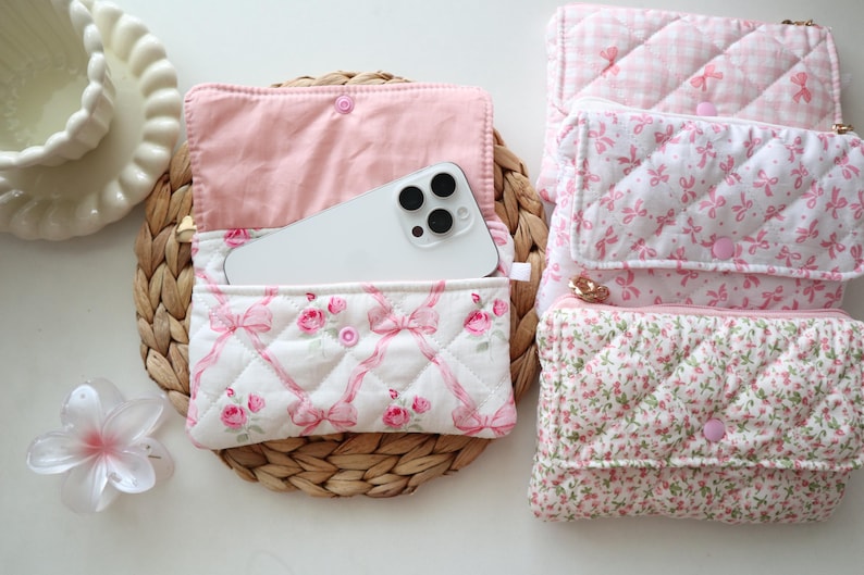 May include: A collection of four rectangular quilted fabric pouches featuring various pink and white patterns including floral prints, bows, and gingham checks. Each pouch has a flap closure with a pink snap button and a soft interior lining.