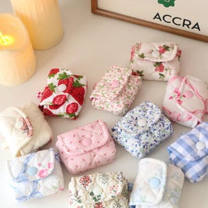 Pu&ograve; includere: Una collezione di piccole pochette in tessuto trapuntato con chiusure a scatto, caratterizzate da vari motivi tra cui fragole, stampe floreali e quadretti vichy blu. Ogni pochette &egrave; rettangolare e dotata di una patta.