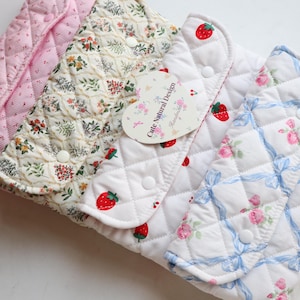 May include: A collection of quilted fabric pouches in various patterns. Designs include pink floral, cream floral, strawberry, and rose patterns. Each pouch has a button closure. A heart-shaped tag reads "Cute Natural Design."
