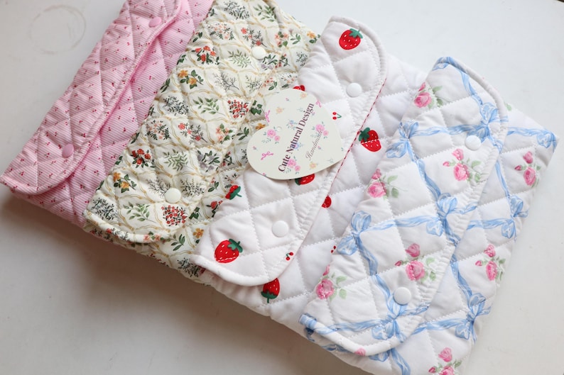 May include: A collection of quilted fabric pouches in various patterns. Designs include pink floral, cream floral, strawberry, and rose patterns. Each pouch has a button closure. A heart-shaped tag reads "Cute Natural Design."