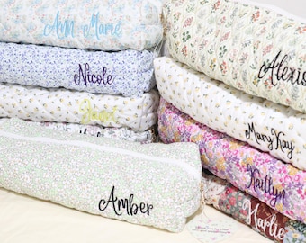 May include: A collection of rectangular quilted fabric pouches featuring various floral patterns in colors including blue, yellow, pink, and green. Each pouch is personalized with embroidered names such as Ann Marie, Nicole, Janet, Amber, Alexis, Mary Kay, Kaitlyn, and Harlie.