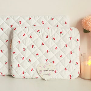 May include: Two white quilted cases with a repeating pattern of red cherries. The cases are different sizes and have a diamond pattern. The smaller case has a gold zipper. A small tag reads "Cute Natural Design Handmade".