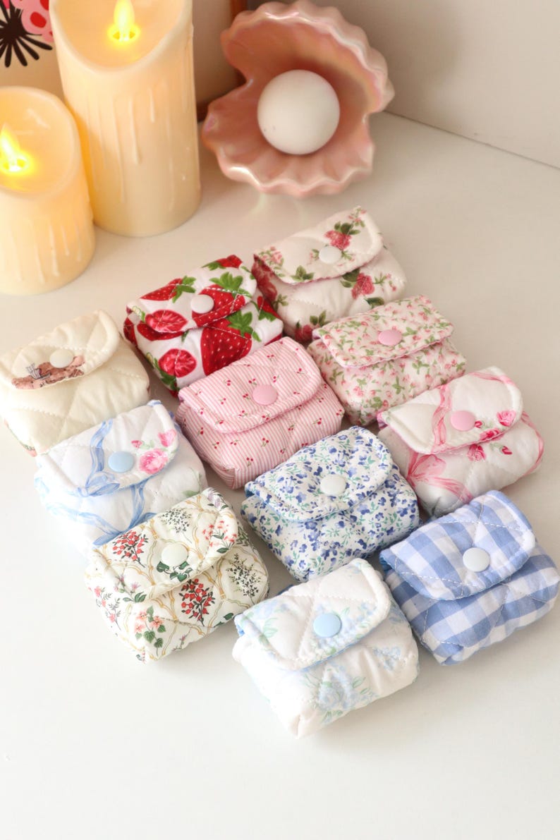 Pu&ograve; includere: Una collezione di piccole pochette in tessuto trapuntato con vari motivi, tra cui fragole, stampe floreali e quadretti vichy blu. Ogni pochette quadrata &egrave; dotata di una patta chiusa da un bottone a pressione in plastica.