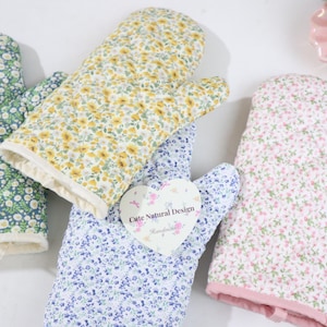 May include: Four floral-patterned oven mitts in shades of green, yellow, blue, and pink. Each mitt features a different floral design, with a heart-shaped tag that reads "Cute Natural Design". The mitts are made of a soft, quilted fabric.