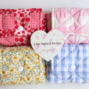 May include: Four quilted fabric pouches in red, pink, yellow, and blue patterns. Each pouch has a button closure. A heart-shaped tag with the text "Cute Natural Design Handmade" is in the center.