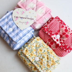 May include: Four quilted fabric pouches in various patterns: blue gingham, pink check, red floral, and yellow floral. Each pouch has a white snap closure. A heart-shaped tag reads "Cute Natural Design Handmade."