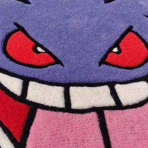 May include: A purple rug featuring a cartoon face with red eyes, a pink tongue, and white teeth. The rug has a jagged outline and a black border, creating a playful and vibrant design. This rug is perfect for a kid's room or a game room.
