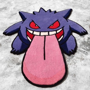 May include: A purple and black rug shaped like a cartoon character with a large pink tongue. The character has red eyes, a wide grin, and pointed ears. The rug is placed on a gray concrete surface.
