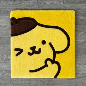 May include: A square, yellow rug featuring a cartoon character's face in brown and black. The rug has a soft, plush texture and a simple, yet recognizable design. The character's face is centered on the rug.
