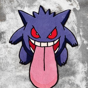 May include: A purple rug shaped like a cartoon character with a wide grin and a long pink tongue. The character has red eyes and a spiky head. The rug is on a gray surface.