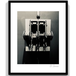 May include: A black and white photograph of a vintage industrial switch with multiple levers. The switch is mounted on a wall and has a simple, functional design.