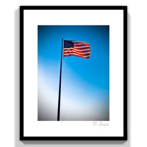 May include: An American flag waving in the wind against a bright blue sky. The flag is red, white, and blue with stars on a blue field. The flag is attached to a tall pole.
