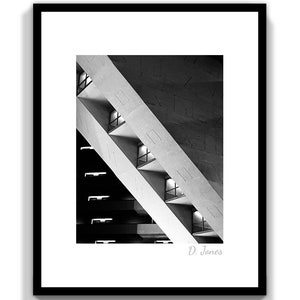 May include: Black and white photograph of a modern building's interior, featuring a geometric pattern of angled concrete walls and rows of windows. The image is signed "D. Jones" in the bottom right corner.