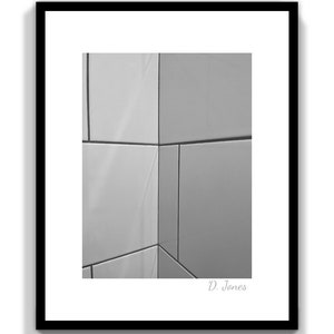 May include: Black and white photograph of a corner of a tiled wall. The tiles are arranged in a simple pattern, creating a geometric design. The image is signed "D. Jones" in the bottom right corner.