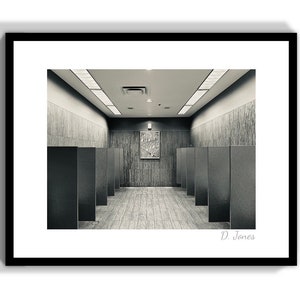 May include: A black and white photograph of a hallway with a series of stalls on either side. The hallway is empty and the stalls are all closed. There is a small piece of art on the wall at the end of the hallway. The photo is signed "D. Jones".