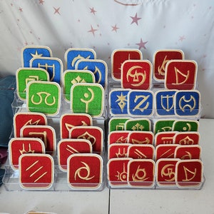 May include: A collection of 24 embroidered patches featuring various symbols in red, blue, and green. The patches are arranged in three rows of eight, each row in a different color. The patches are displayed on a white surface.
