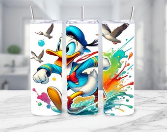 Peut inclure: Un gobelet blanc avec un motif de peinture éclaboussé coloré. Une image de bande dessinée de Donald Duck est présentée sur le gobelet, portant une chemise de marin bleue et une casquette. Il court avec une expression déterminée sur son visage.