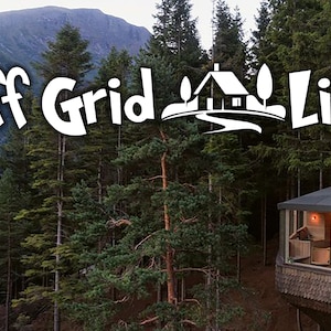 Könnte beinhalten: Luftaufnahme einer Hütte im Wald mit dem Text "Off Grid Life". Die Hütte ist in die Bäume gebaut und hat ein einzigartiges Design mit einem dunklen Dach und großen Fenstern. Die Umgebung ist voller hoher grüner Bäume und einer Bergkette im Hintergrund.