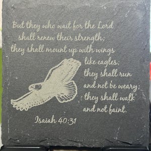 Könnte beinhalten: Ein dunkelgrauer Schieferuntersetzer mit geätztem Text und einer Adlergrafik. Der Text lautet: "Aber die auf den HERRN harren, kriegen neue Kraft...Jesaja 40,31". Der Adler ist mit ausgebreiteten Flügeln dargestellt.
