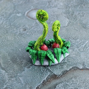 May include: A miniature green and yellow plant with red berries, set on a gray base. The plant is made of plastic and is a tabletop decoration.