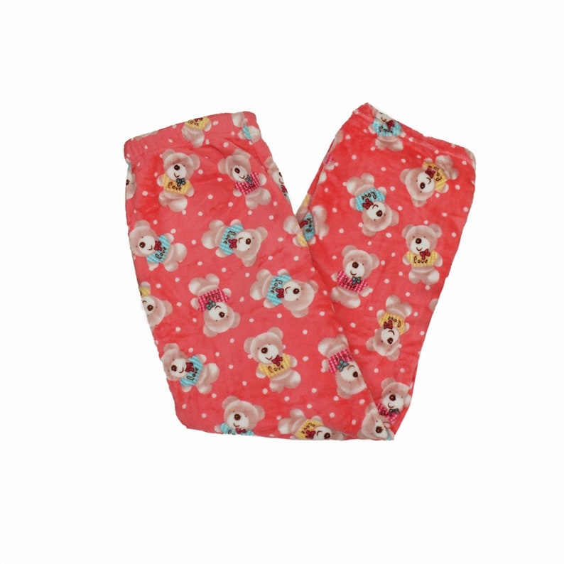 Puede incluir: Pantal&oacute;n de pijama rosa con un patr&oacute;n de lunares blancos y un estampado repetido de osos de dibujos animados que llevan jers&eacute;is de colores.