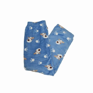 Puede incluir: Pantal&oacute;n de pijama azul con un estampado de huellas de perro y cara de perro blancas y marrones.