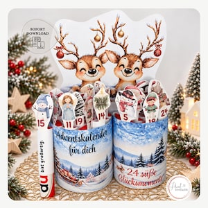 Puede incluir: Un set de calendario de adviento DIY con dos recipientes cilíndricos decorados con paisajes invernales, renos y recortes numerados de muñecos de nieve, ángeles y elfos. El texto dice Adventskalender für dich, 24 süße Glücksmomente y du bist großartig.