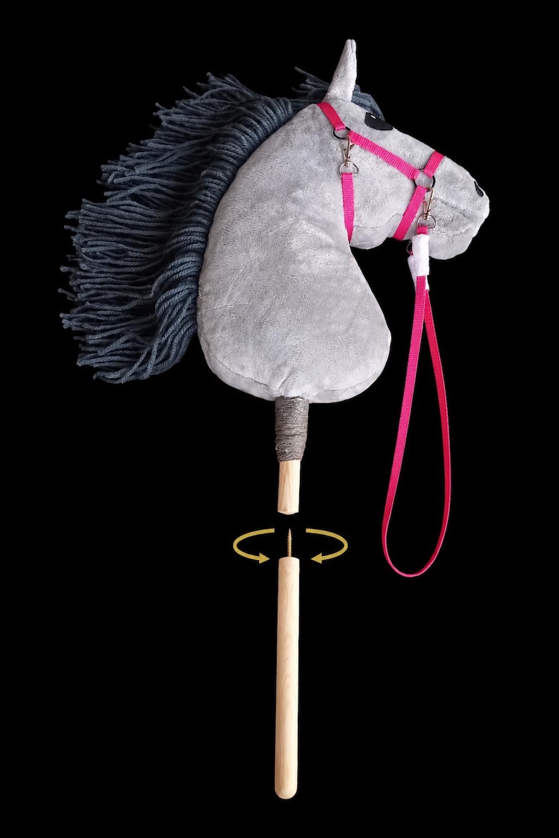 May include: A grey plush hobby horse with a dark grey yarn mane, featuring a bright pink bridle and a long pink lead. The horse head is attached to a detachable wooden stick handle, shown separated with a visible metal screw and yellow arrows.