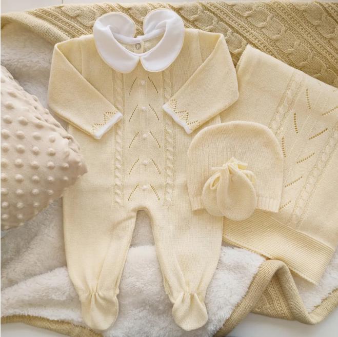 May include: A pale yellow baby clothing set, including a romper, hat, mittens, and blanket. The romper has a white collar and decorative stitching. The blanket and hat have a matching knit pattern. The set is displayed on a soft, textured surface.