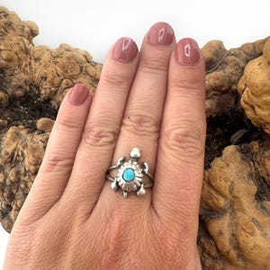 May include: A silver ring shaped like a turtle with a small, round, bright blue turquoise stone set in the center of its shell. The metal has a polished finish with detailed markings on the turtle's limbs and head, creating a distinct design.