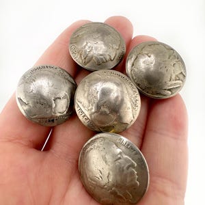 May include: Five silver-coloured United States five-cent coins. Four coins feature the profile of a Native American and the text United States of America, while one coin displays the profile of a person and the text Liberty and the year 1942.