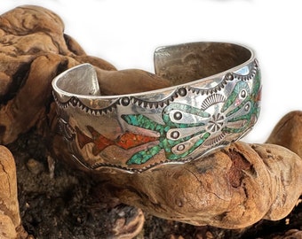 May include: A silver bracelet with turquoise and coral inlay. The bracelet features a geometric design with a central motif of a stylized flower.