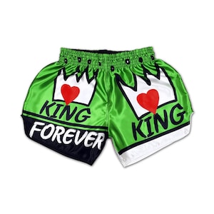 Puede incluir: Shorts de Muay Thai verde y blanco con cintura negra. Los shorts presentan un gráfico de dos coronas con corazones en su interior y el texto "King Forever" y "King".