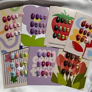 Peut inclure: Assortiment de motifs d'art d'ongles colorés sur des cartes d'affichage. Chaque carte présente un thème différent, notamment des fleurs, des fraises et des motifs abstraits. Les motifs comprennent diverses formes, couleurs et illustrations mignonnes.