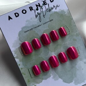 Könnte beinhalten: Satz mit zehn pinkfarbenen Press-on-Nägeln mit glänzendem Finish. Die Nägel werden auf einer weißen Karte mit dem Text "Adorned by Debora" und "handmade | reusable | customizable" angezeigt.