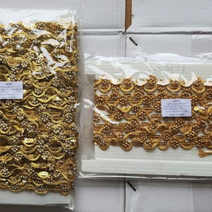 May include: Two packages of gold-colored decorative trim. The trim has a wavy design with sequins and small, round beads. The trim is packaged in clear plastic. One package is larger than the other.