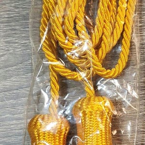 May include: A pair of 100-inch long, gold military cords with 5-inch tassels on both ends. The cords are packaged in a clear plastic bag with a label that reads "#927A 100" L, 5/4" Dia Flag Gold Military Cord with 5" Tassels on both ends Color: YELLOW GOLD | http://www.indianproduct.com/ Made in India".