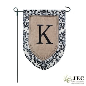 May include: A garden flag with a black and white damask pattern and a burlap-textured shield. The shield features the letter "K" in black. The flag is attached to a black metal stake for easy display in a garden or yard.